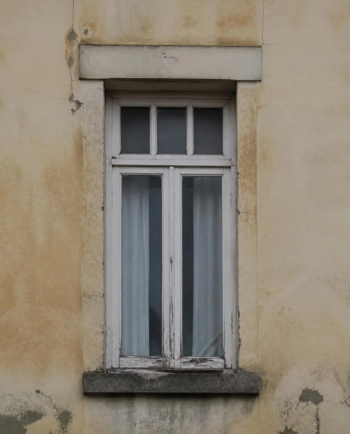 Ventana antigua de madera con la pintura desconchada en una fachada con humedades