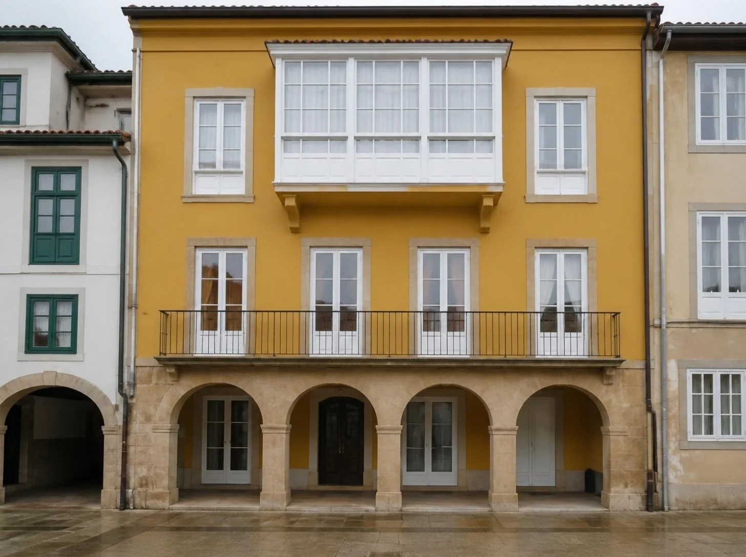 Fachada ocre renovada con galería acristalada blanca y soportales en Avilés